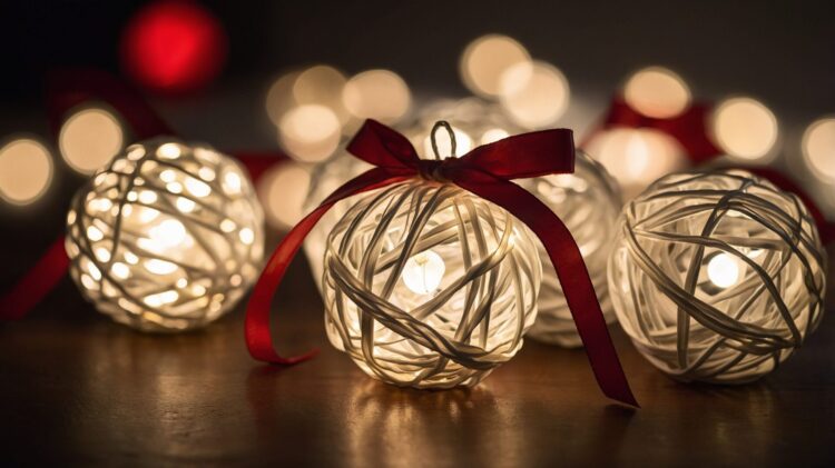 White wicker balls with red ribbons and light bulbs, arranged as festive Christmas decorations on a table.