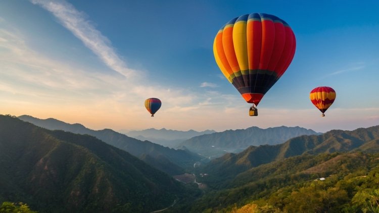 Colorful hot air balloons float above green mountains and forests under a clear blue sky with sunlight shining on them.