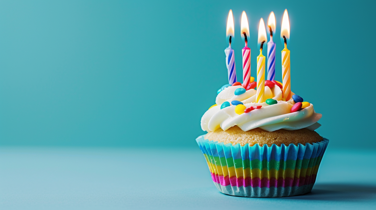 Colorful birthday cupcake with lit candles on a blue background, symbolizing celebration with copy space.