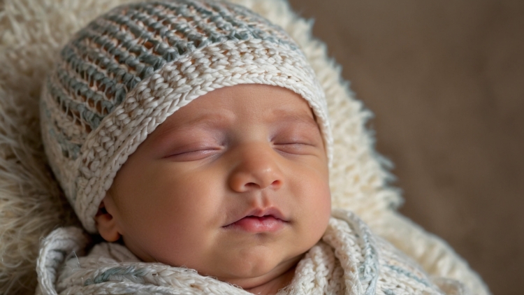 Sleeping newborn in knitted cap, close-up with sharp facial focus and soft beige bokeh background