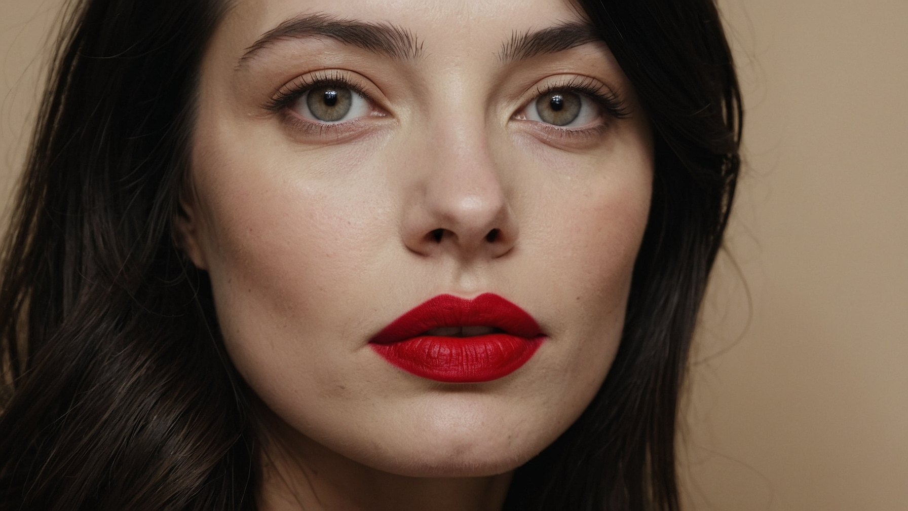 Close-up portrait of woman with long dark hair, bright red lips, subtle eye makeup, and clear skin against beige background. Close-up portrait of woman with long dark hair, bright red lips, subtle eye makeup, and clear skin against beige background.