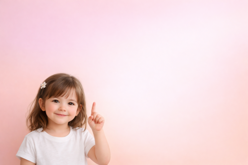 Young smiling girl with brown hair wearing a white t-shirt and a flower hairpin, pointing upwards with one finger against a pink gradient backdrop