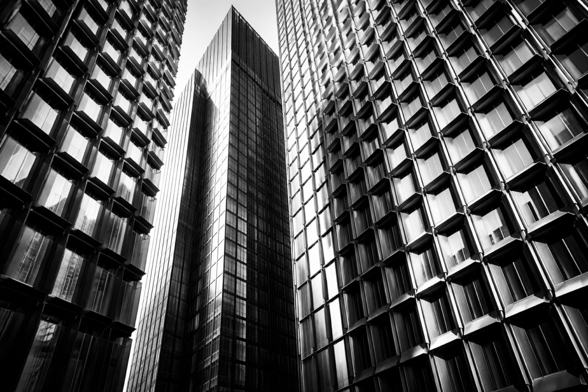 Monochrome photo showing tall modern skyscraper buildings with reflective glass surfaces and geometric window patterns