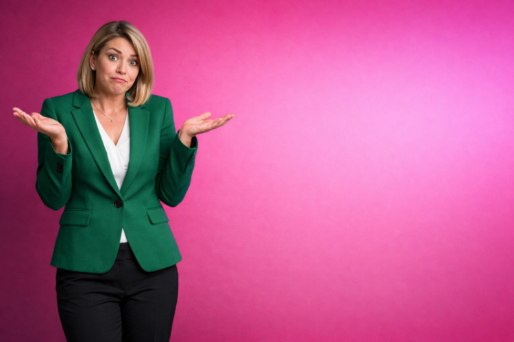 Portrait of a businesswoman in a green blazer showing a confused expression and open palms against a pink background