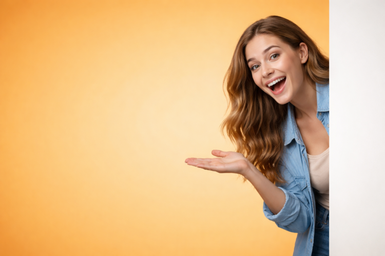 Excited young woman with long wavy hair smiling and pointing to her open palm against an orange background