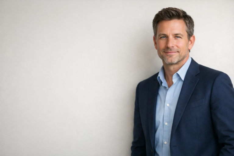 Professional middle-aged man in blue suit and light blue shirt smiling with soft confident expression against a neutral background
