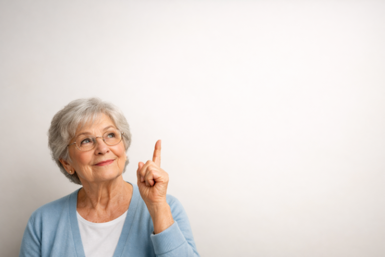 Senior woman with gray hair and glasses wearing a blue cardigan pointing upwards with a thoughtful expression