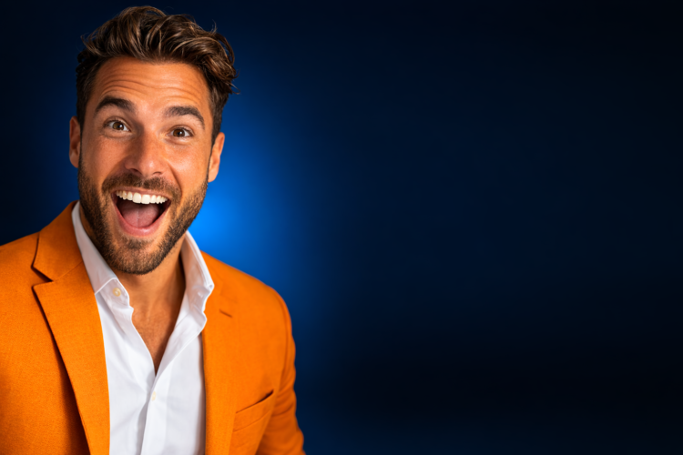 A happy young man wearing an orange blazer and a white shirt, with an expressive, excited facial expression against a dark blue background