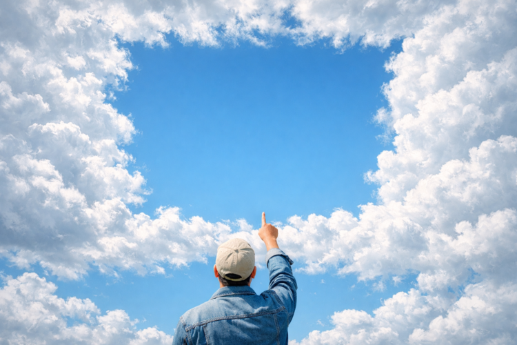 Back view of a man in a denim jacket and cap pointing up at a square-shaped cloud frame against a bright blue sky