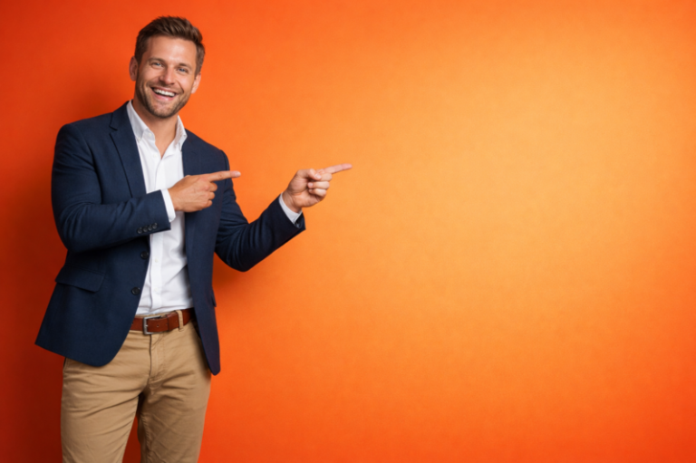 Confident young businessman in blazer and shirt smiling while pointing to empty orange background space