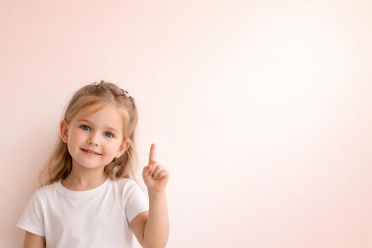 Happy young blonde girl in white shirt smiling and raising her index finger on pastel pink background