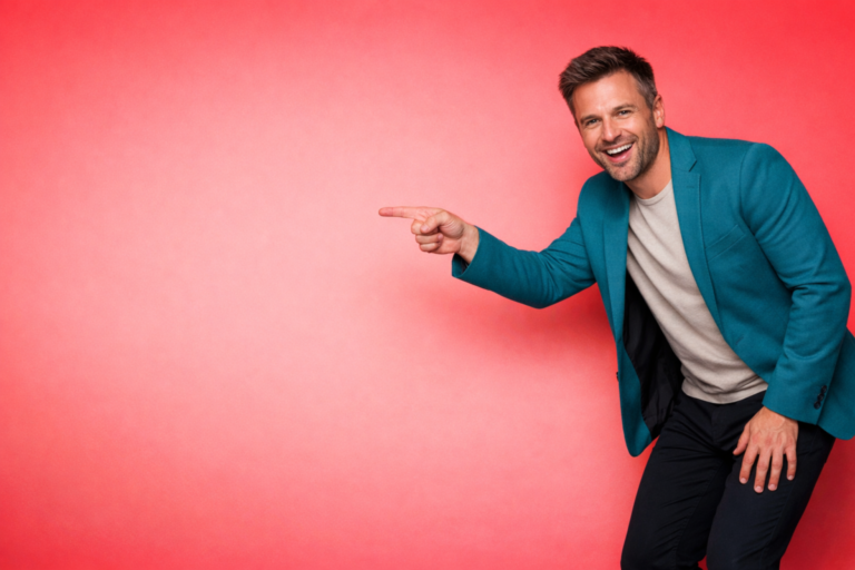 Cheerful man in teal blazer and light shirt pointing to the left on a smooth red background