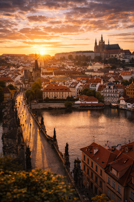 Golden sunset over Prague's Charles Bridge with silhouettes of historic buildings and a river reflecting the warm light