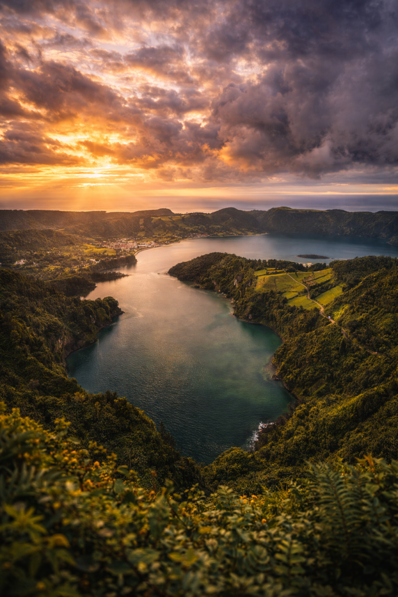 View of a tranquil mountain lake surrounded by green forests and hills under a dramatic cloudy sunset sky