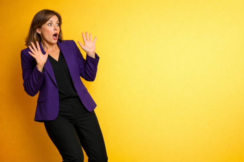 Shocked businesswoman with hands raised, wearing a purple blazer and black outfit, standing against a yellow backdrop