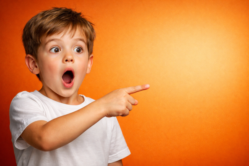 Young boy with wide eyes and open mouth pointing excitedly to the right on a vibrant orange background