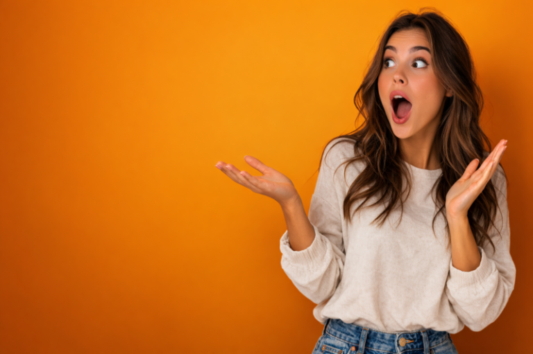 Young woman with long hair showing a surprised expression with open mouth and raised hands on orange background