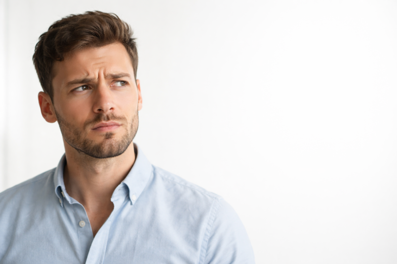 Portrait of a young man with light beard and blue shirt looking thoughtfully to the side against a white background