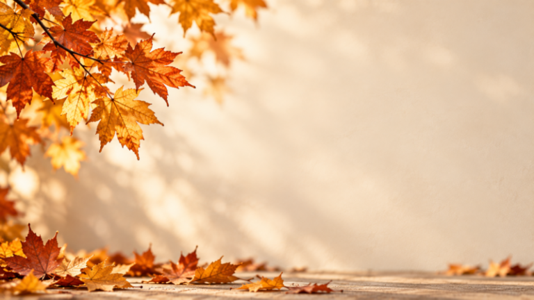 Golden orange maple leaves hanging and scattered on rustic wooden surface with blurred beige background, creating warm autumn ambiance